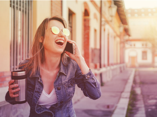 woman laughing one the phone holding a cup of coffee